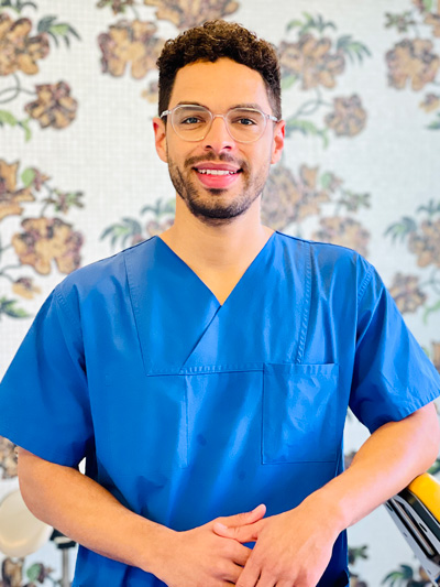 Dr. Surian Herrmann, Fachzahnarzt für Oralchirurgie stehend vor Tapete